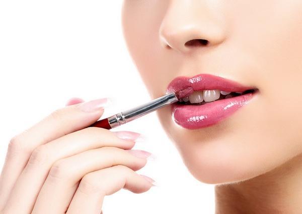beautiful young woman applying lips makeup with cosmetic brush, white background, copyspace