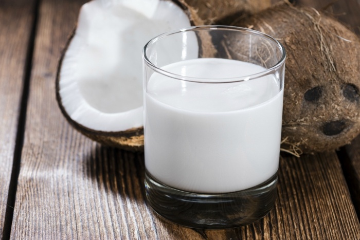 Coconut Milk in a glass on dark wooden background (close-up shot)