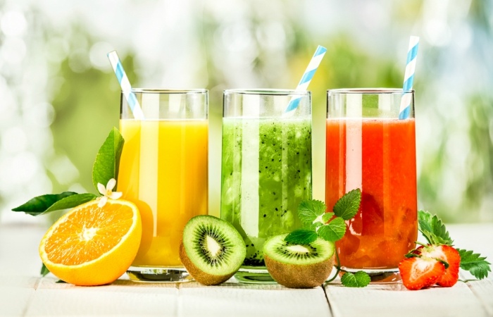 Delicious array of fresh fruit juices served in tall glasses made from liquidised orange, kiwifruit with peppermint, and strawberries for healthy summer treats rich in vitamins