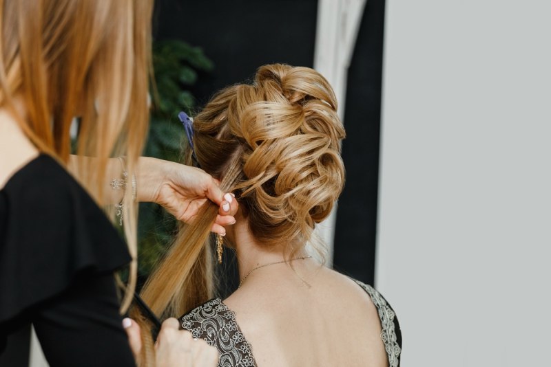 Hairdresser makes upper bun wedding hairstyle close-up on sandy blond hair of beautiful woman