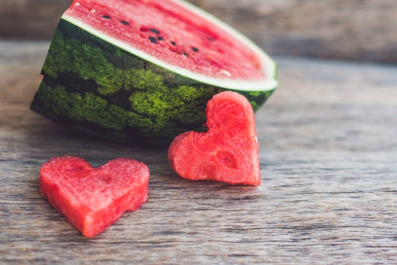 Healthy watermelon smoothie with mint, a piece of watermelon, hearts and a striped straw on a wood background.