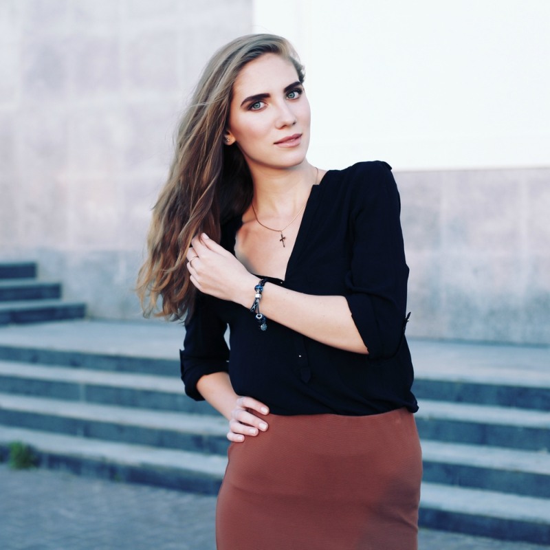 Portrait of a beautiful girl in a black blouse and straight brown skirt in fashionable jewelry with natural long hair