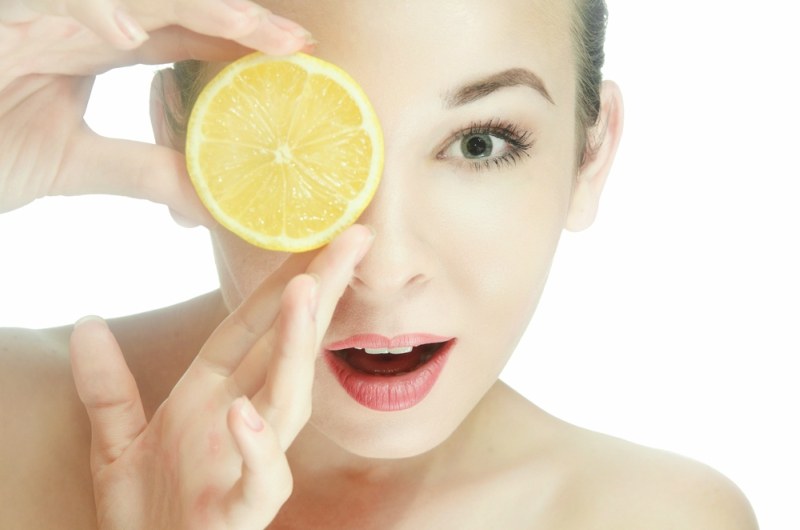 Portrait of a young woman with one halves of a lemon near the lips. Mouth open. Hands near the face. Horizontal photo
