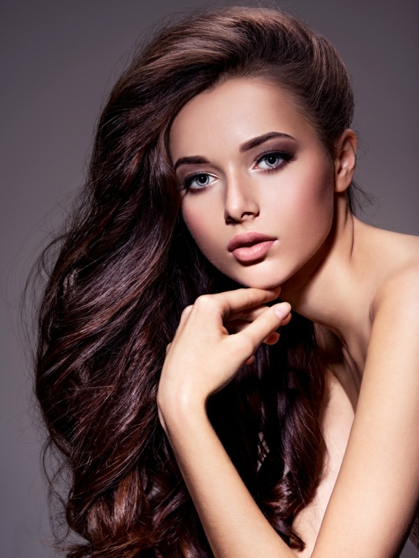 Portrait of the beautiful young woman with long brown hair posing at studio over dark background
