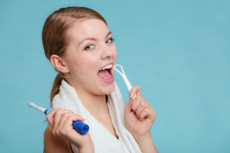 Pretty young girl with electric brush and tongue cleaner. Happy woman cleaning her oral cavity caring about dental health.