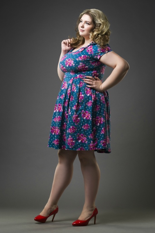Young beautiful blonde plus size model in dress and shoes, xxl woman on gray studio background, full length portrait