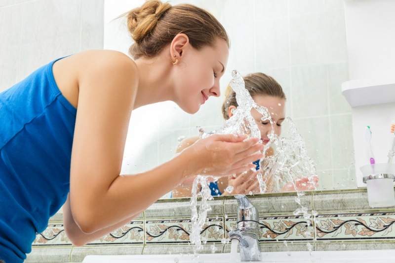 Young woman washing her face with clean water in bathroom