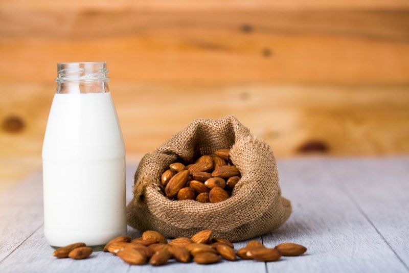 almond milk in bottle with almonds in sackcloth on woodene background with copy space