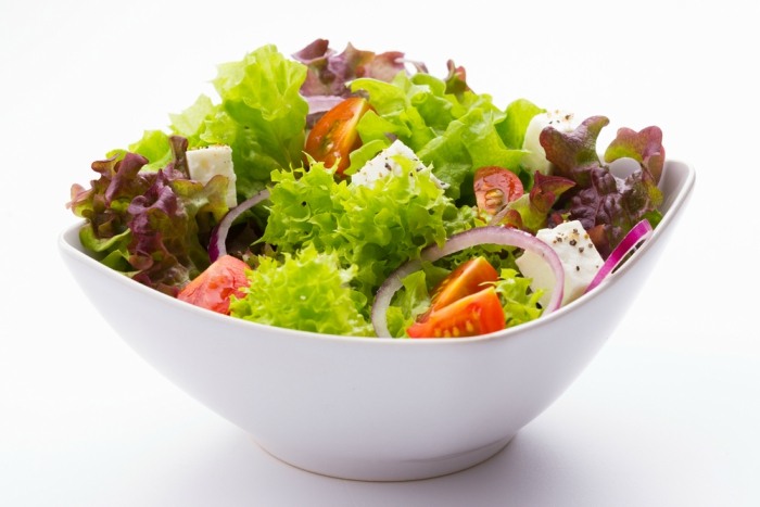 mixed vegetable salad with tomatoes, onions and feta cheese in a white bowl on white background