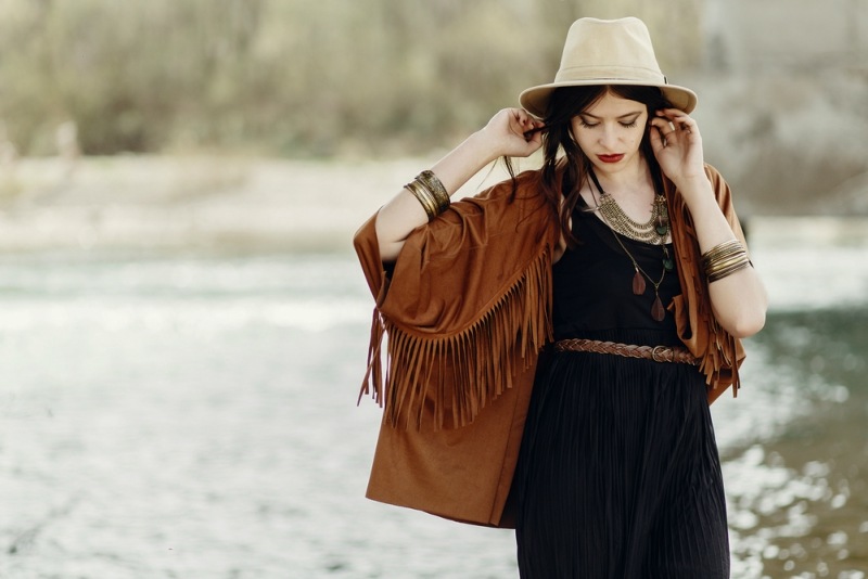 stylish hipster gypsy boho woman posing in hat with windy hair, in fringe poncho and accessory. traveler girl look. summer travel. atmospheric moment. space for text. sensual portrait