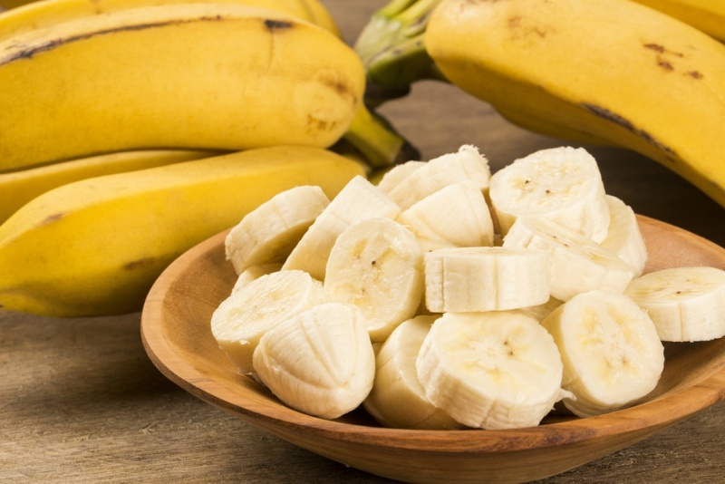 A branch of bananas and a sliced banana in a pot over a table.