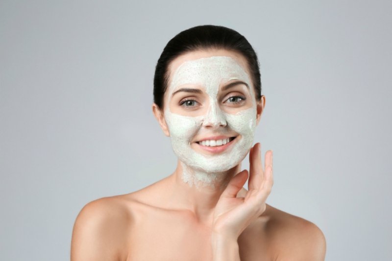 Beautiful young woman applying scrub mask on face closeup