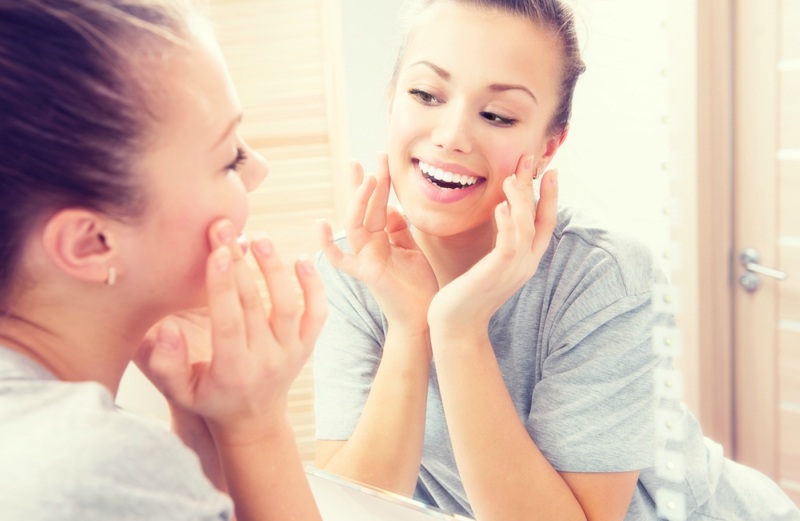 Beauty skin care. Young beautiful teenage girl touching her face before the mirror, enjoying her clean skin.