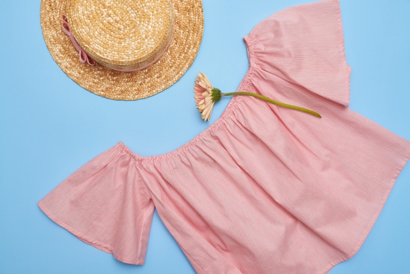 Overhead shot of an off-the-shoulder swing blouse with straw hat. Summer feminine outfit. Straw hat, blouse and flower on blue