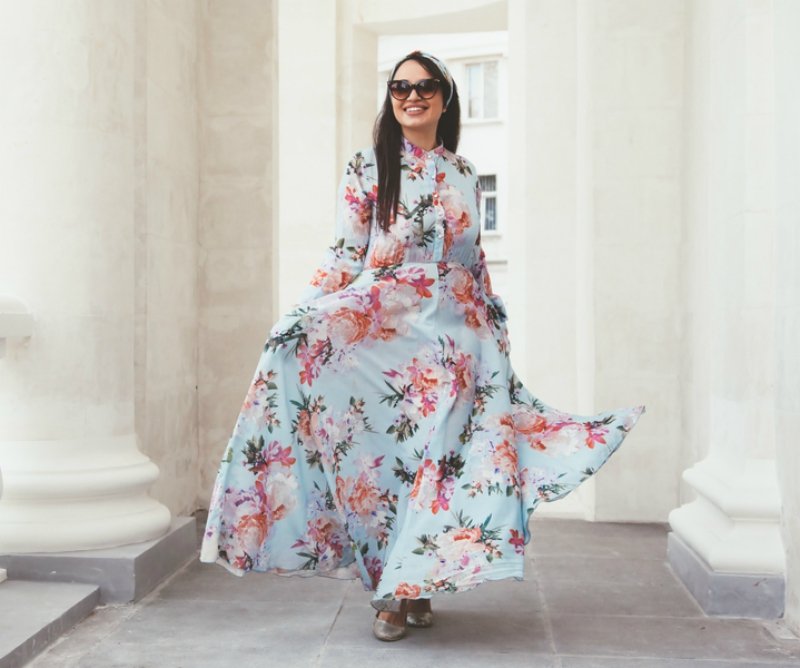 Plus size model wearing floral maxi dress posing on the city street. Young and fashionable overweight woman walking around town.