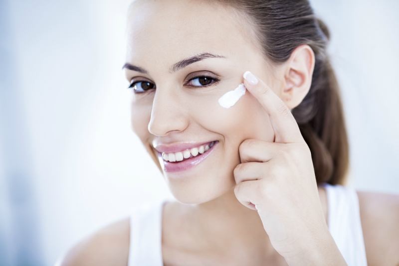 Smiling young woman applying face cream.