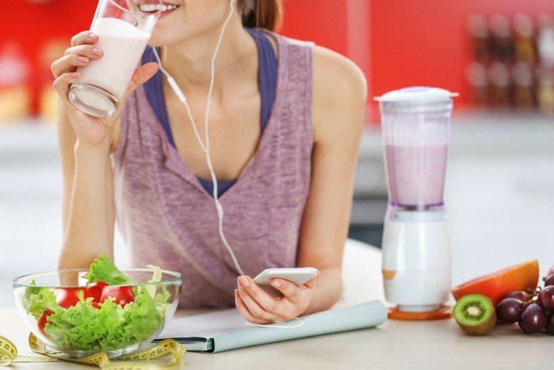 Woman drinking a healthy cocktail and listening to music in the kitchen