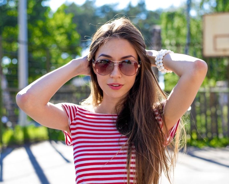 Young beautiful woman looks bright sunglasses passionately look, long hair beautiful makeup, wearing a red shirt in the park. Summer city portrait fashion street style, stunning views.