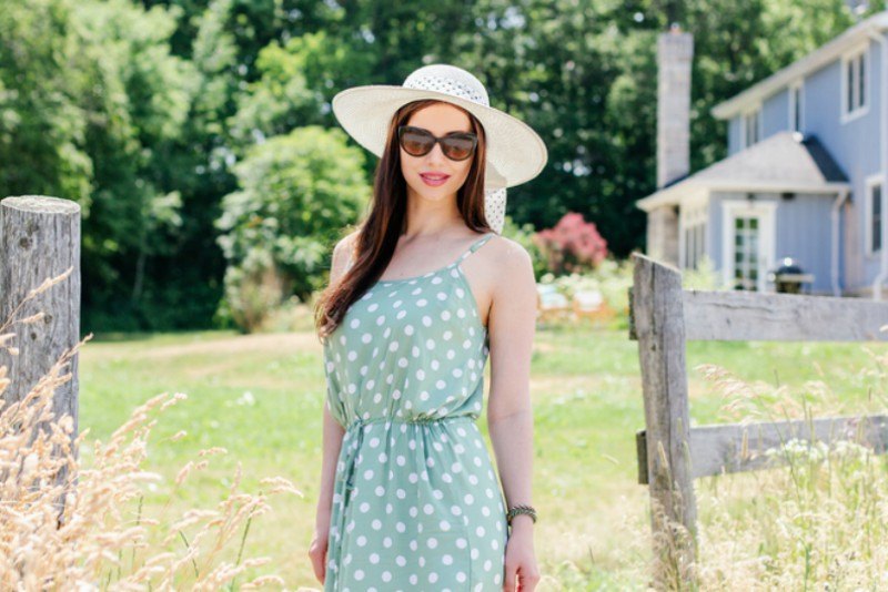 Young woman in sunglasses wearing maxi dress and a hat at a farm