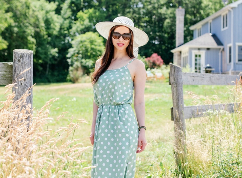 Young woman in sunglasses wearing maxi dress and a hat at a farm
