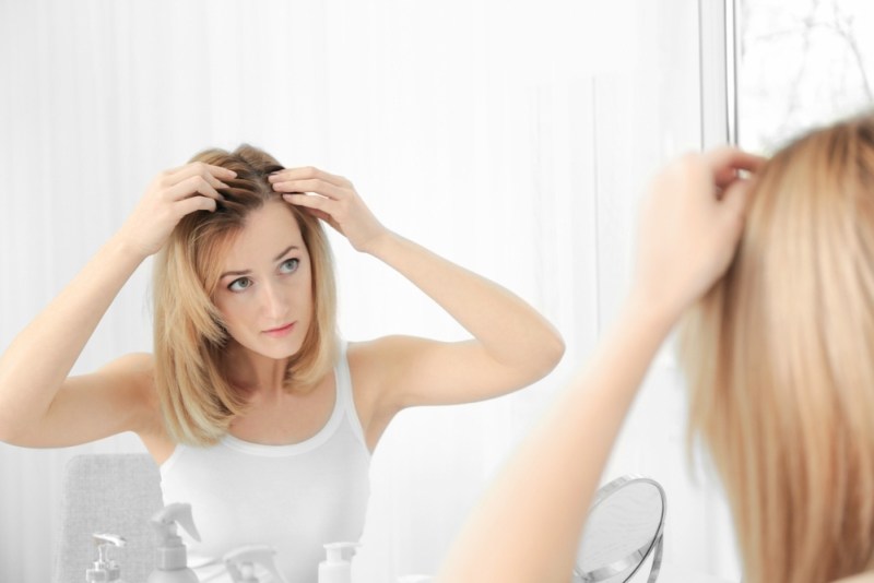Young woman with hair loss problem looking in mirror at home