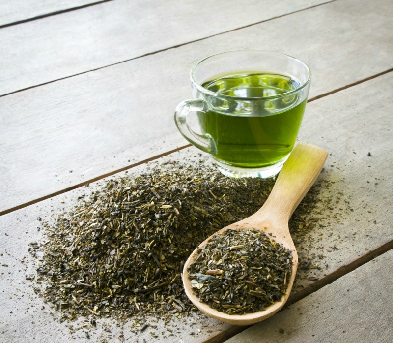 cup of green tea and spoon of dried green tea leaves on wooden background