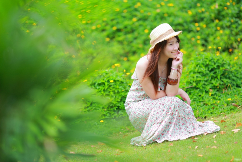 Asian beautiful young girl,wear floral maxi dress and hat, sitting on the ground at spring