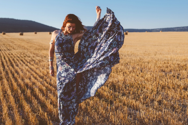 Beautiful model wearing summer cotton maxi dress and jewelery posing in autumn field with hay stack. Boho style clothing and jewelry.