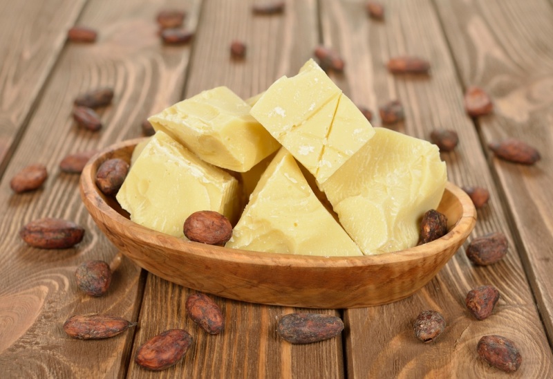 Natural cocoa butter in a wooden bowl on a brown background
