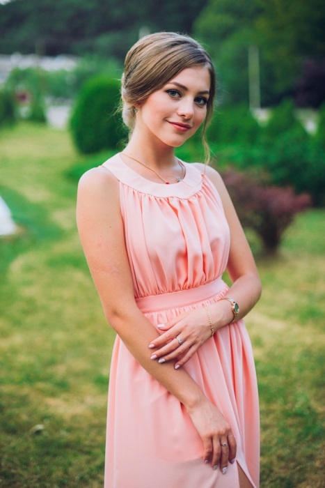 Pretty young girl with in a park with flowers in hand, a bridesmaid in a pink maxi dress