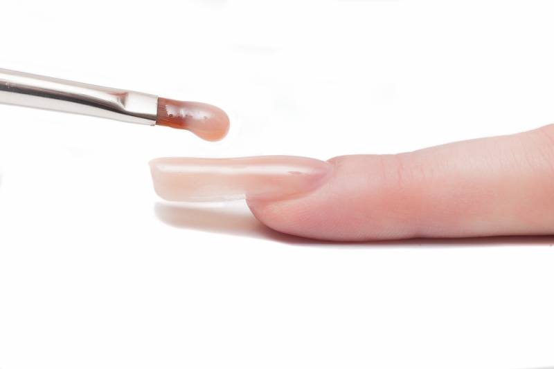 Professional manicurist applying liquid acrylic to nail extensions. macro