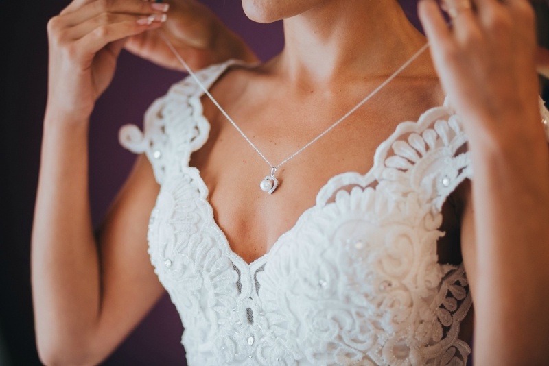 The bride in a white dress putting on a necklace around his neck