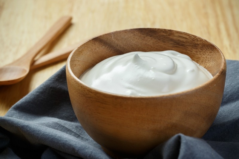 Yogurt in wooden bowl on wooden background with blue cotton and wooden spoon
