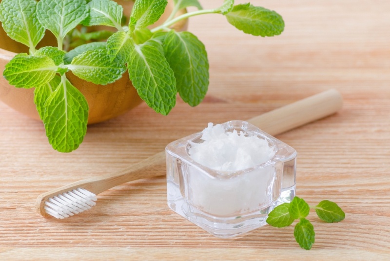 alternative natural toothpaste coconut oil and wood toothbrush closeup, mint on wooden background
