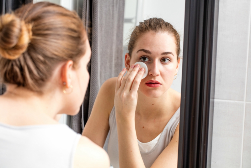 portrait of a beautiful young woman removing her makeup with a cotton swab in front of a home mirror for skin cleansing, purity and beauty routine, real people