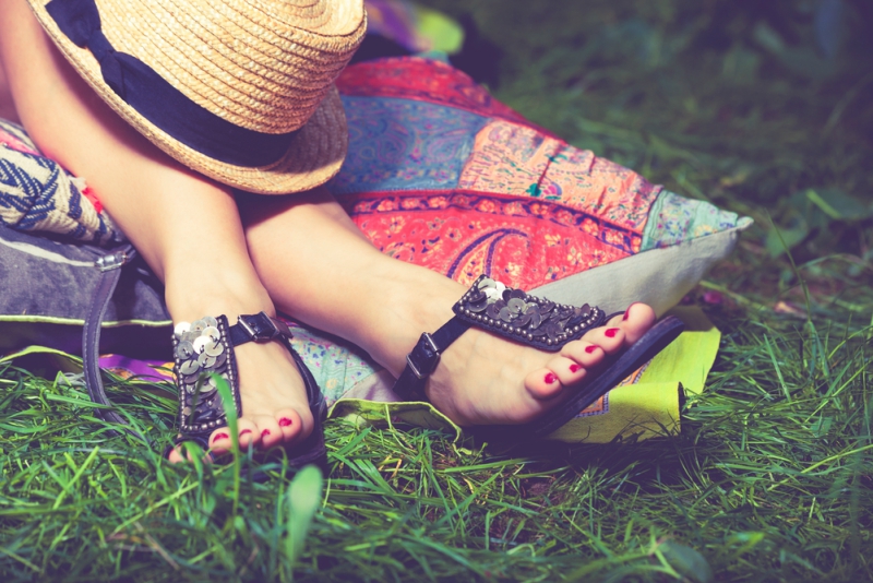 woman feet on grass in flat summer sandals lean on pillows hat lay on legs